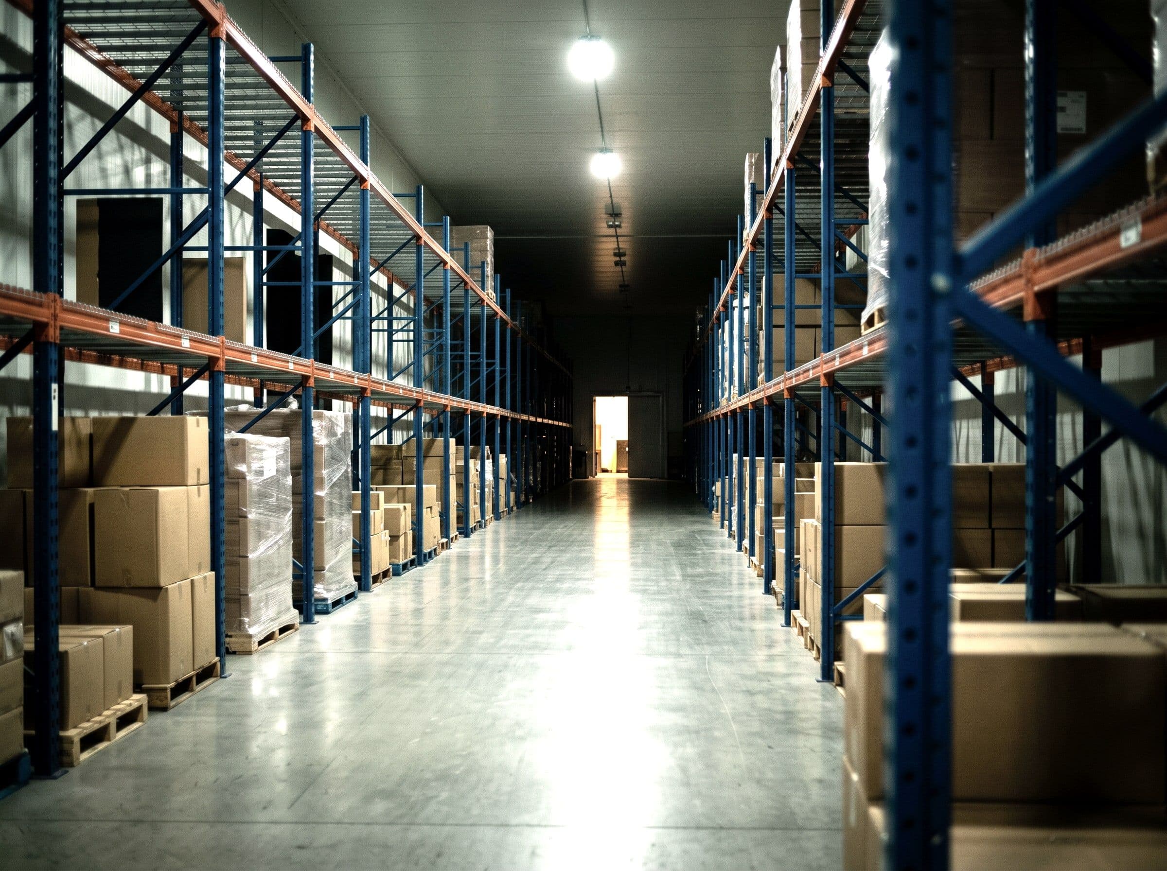 An aisle between pallet racking in a distribution warehouse at night, the floor recently scrubbed